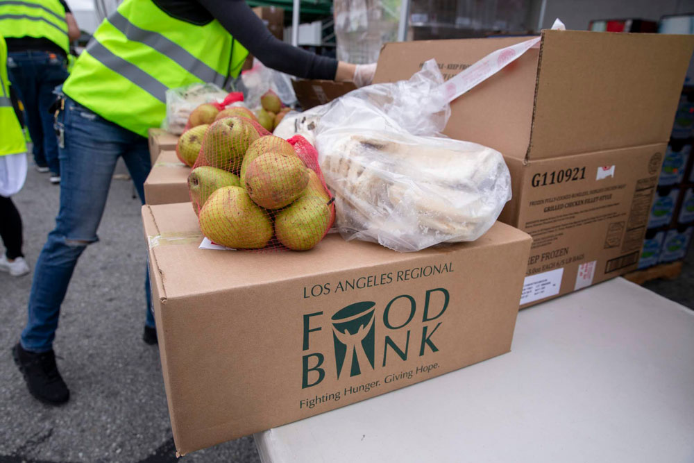 one-time-donation-lafb At a Los Angeles Regional Food Bank event, volunteers clad in high-visibility vests distribute boxes filled with fresh produce. The Los Angeles Regional Food Bank's logo adorns the boxes, which brim with juicy pears and ripe bananas, all neatly arranged on tables.