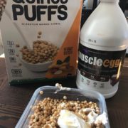 la-food-bank_my-favorite-meal-MyFavoriteMeal-6-180x180 A container filled with quinoa puffs and yogurt sits on a table. Behind it, a box labeled "Quinoa Puffs" and a container marked "MuscleEgg" are neatly aligned, reminiscent of the variety you'll find at the Los Angeles Regional Food Bank. Quinoa puffs spill from the box into a bowl on the packaging.
