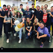la-food-bank_my-favorite-meal-Wefeedla-1-180x180 A group of people pose indoors, smiling at the camera. One person stands in front holding balloons and wearing a colorful hat. Everyone appears relaxed and happy, suggesting a celebratory occasion at the Los Angeles Regional Food Bank. The background features industrial elements.
