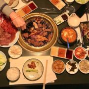 la-food-bank_my-favorite-meal-MyFavoriteMeal-5-180x180 A table with various Korean barbecue dishes, including grilled meat on a central grill, side dishes like kimchi, rice, lettuce, sauces, and a bubbling hot pot. A hand turns the meat on the grill—a feast reminiscent of flavors supported by initiatives like the Los Angeles Regional Food Bank.