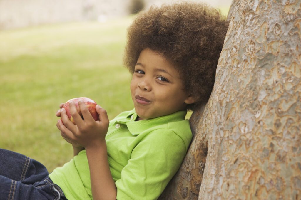 young boy leaning by a tree holding an apple