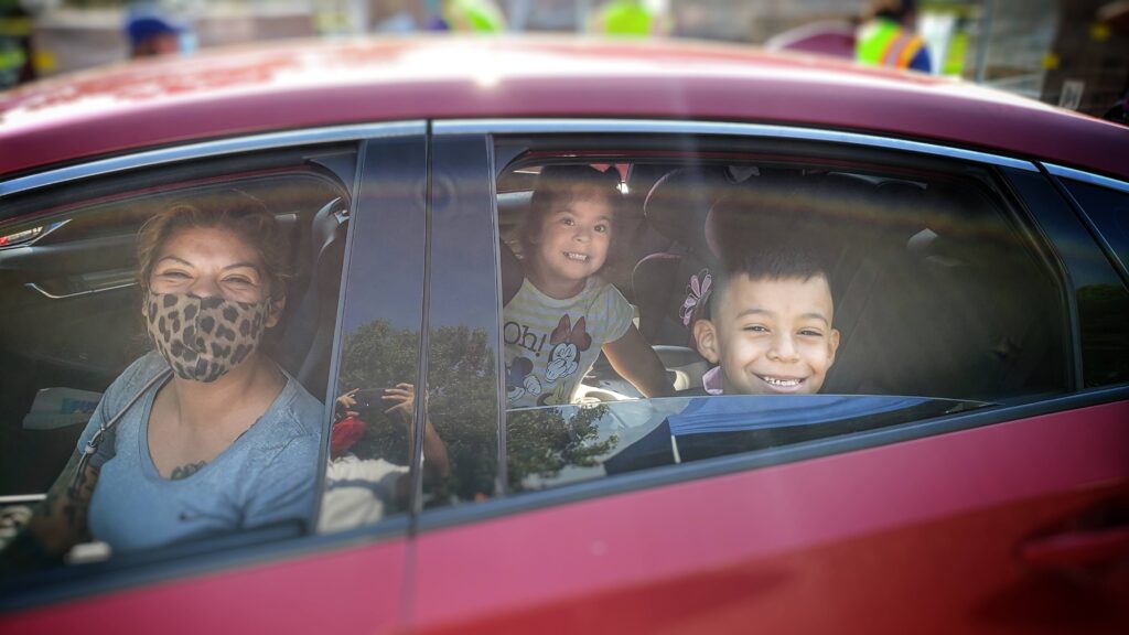 A family of three park and pause for a photo at an emergency food distribution in Compton, hosted by the Los Angeles Regional Food Bank.