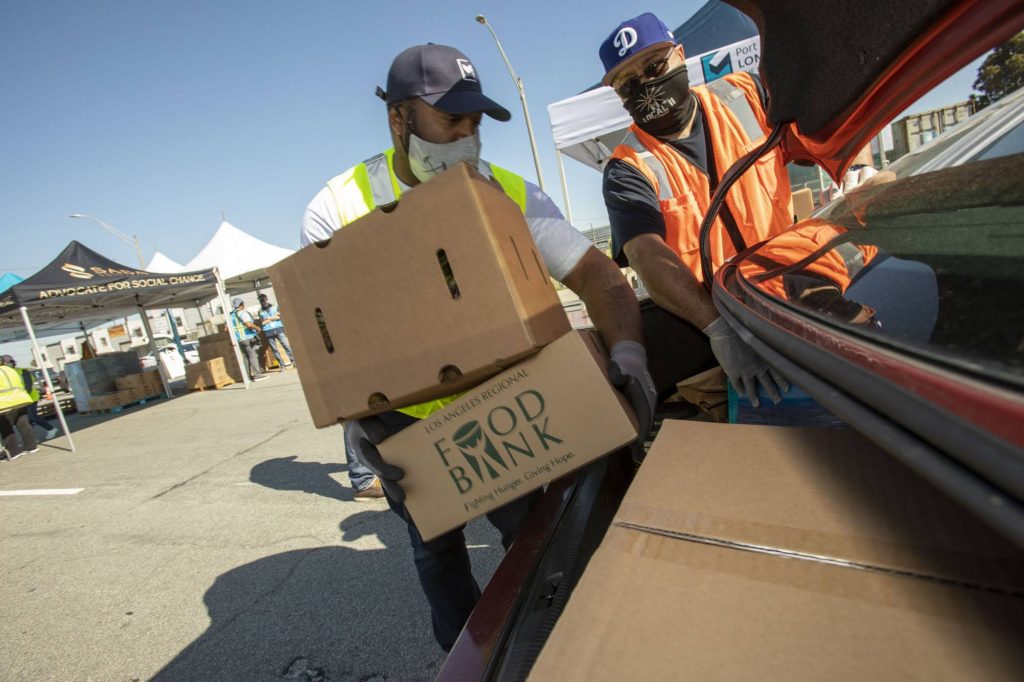 Two volunteers load up a trunk with food kits at a drive-through food distribution hosted by the LA Regional Food Bank.