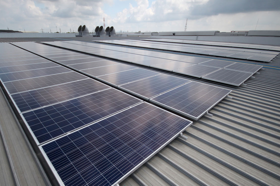 A series of solar panels are installed on the rooftop of the Los Angeles Regional Food Bank under a partly cloudy sky. The panels, arranged in neat rows, reflect light efficiently.