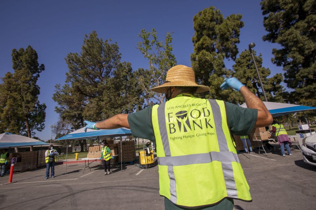 A back view of a LA Regional Food Bank employee directing traffic at a drive-through food distribution in South Gate, CA.