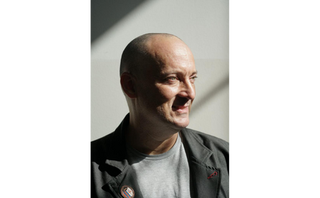 A person with a shaved head, representing the Los Angeles Regional Food Bank, is wearing a jacket and shirt, looking to the side as light casts a shadow behind them.