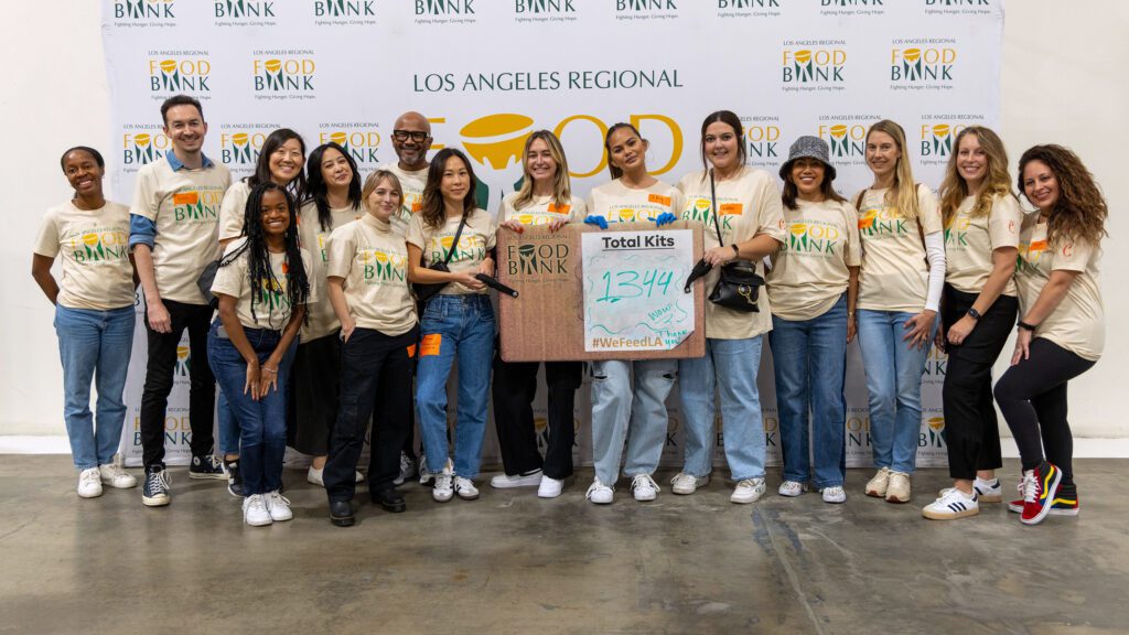 A group of diverse people in matching T-shirts poses at the Los Angeles Regional Food Bank event, proudly holding a sign that reads 