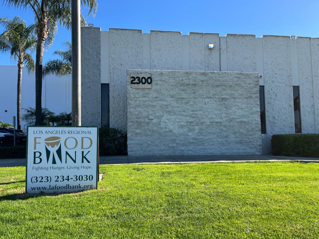 A building with palm trees showcases a sign for the Los Angeles Regional Food Bank, complete with their logo and the inspiring slogan 