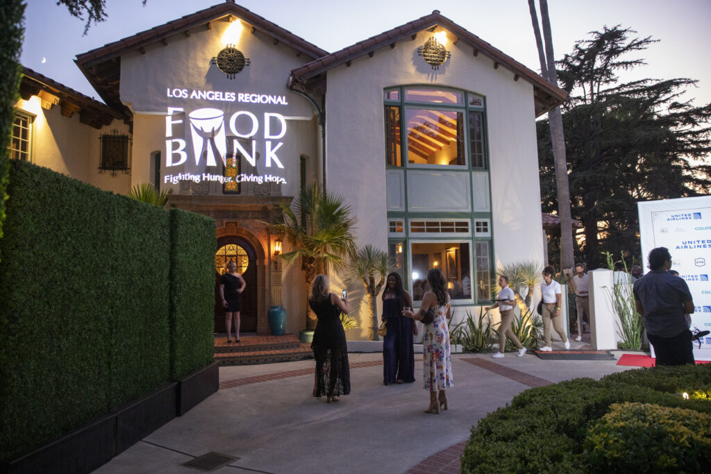 Elegantly dressed attendees gather outside a two-story building, the 