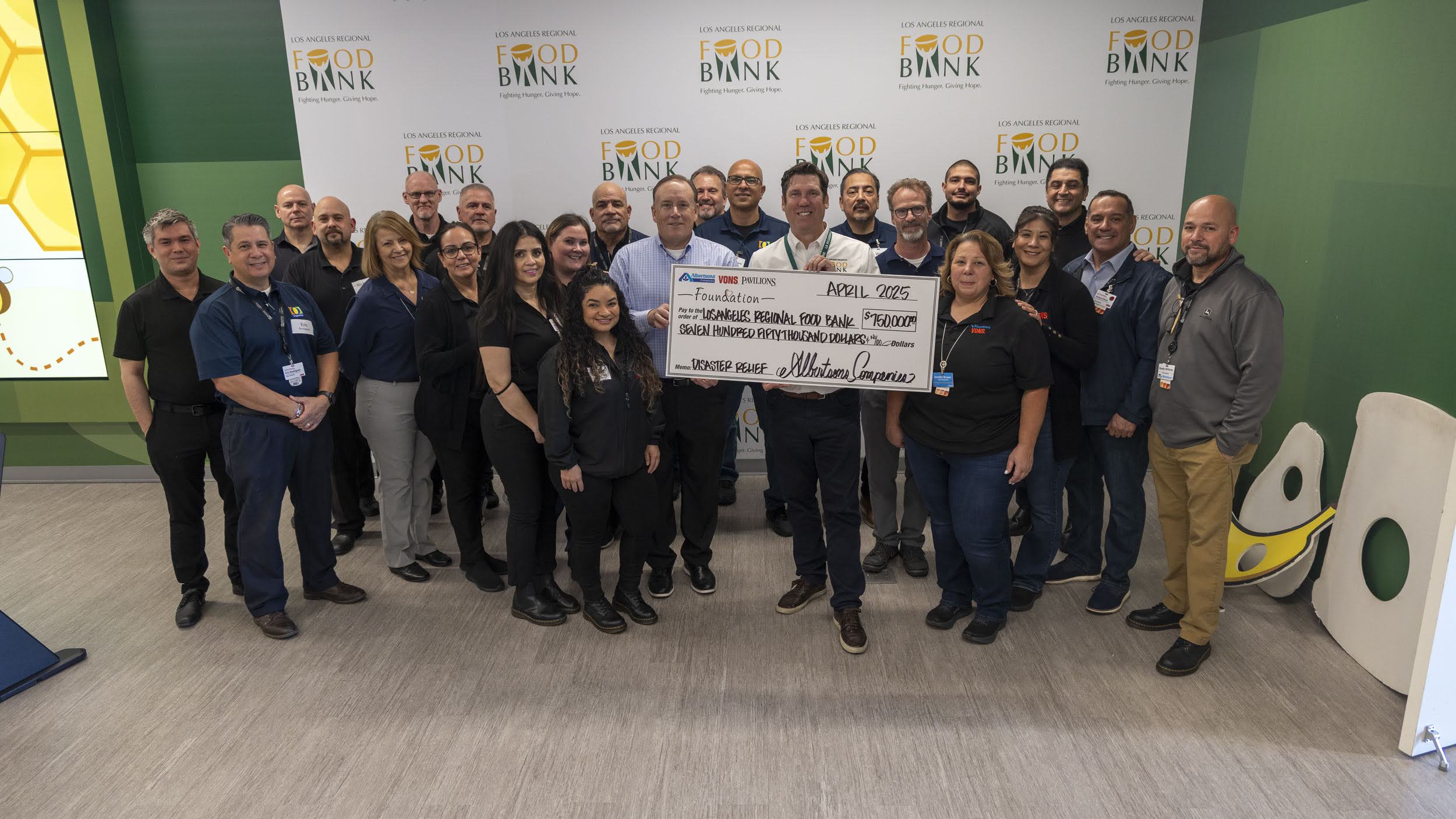 A group of people stands proudly in front of a banner emblazoned with "Food Bank," holding a large check. Smiling at the camera, they embody the spirit of community and support in this vibrant indoor setting.