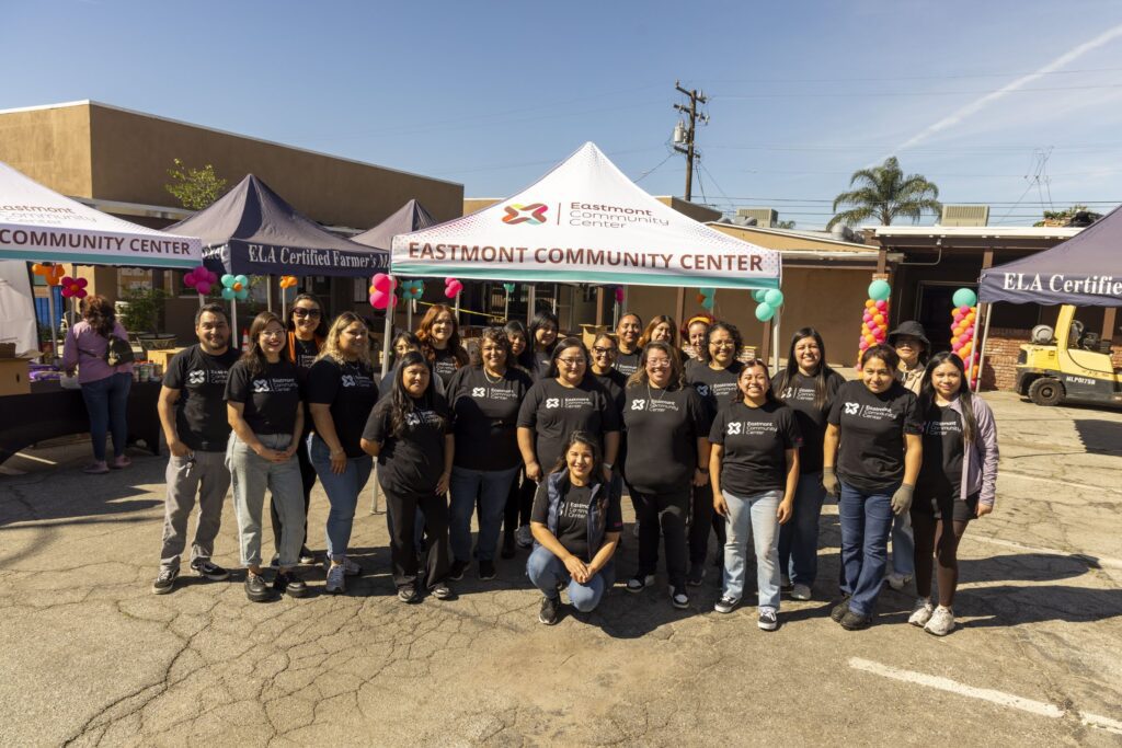 A group of people wearing matching black T-shirts pose and smile in front of tents labeled 