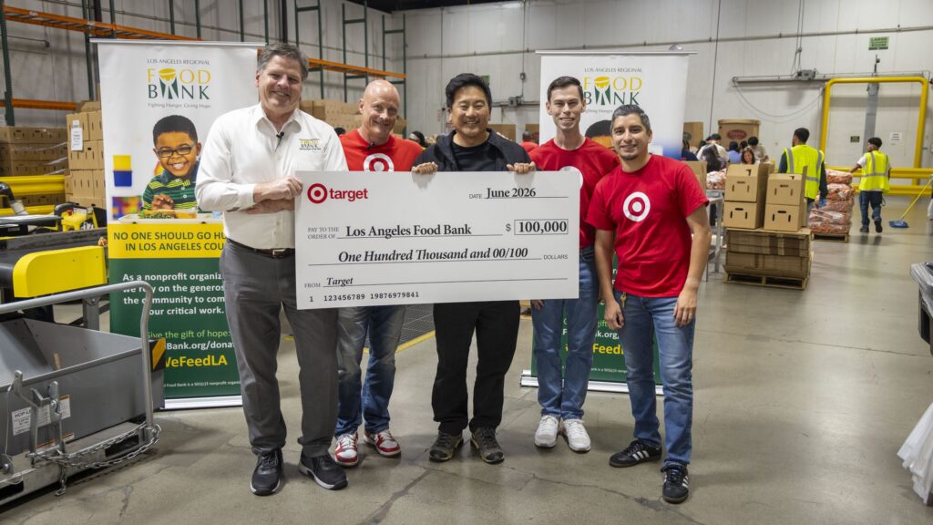 Five people, including a volunteer, smiling and holding a large $100,000 check made out to the Los Angeles Food Bank from Target. They stand in a warehouse with food bank banners and boxes in the background.