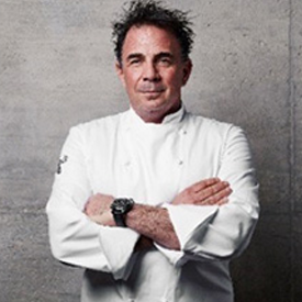 foodbank-Josiah-Citrin-275x275-v1 A chef in a white jacket stands against a gray wall with arms crossed, embodying his passion for culinary arts and community service at the Los Angeles Regional Food Bank. With dark, curly hair and a watch on his left wrist, he represents dedication and excellence in his field.
